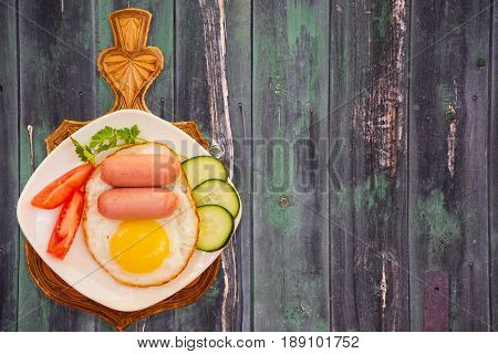 Breakfast of scrambled eggs and mini sausages with vegetables on white plate on gray wooden table vintage top view