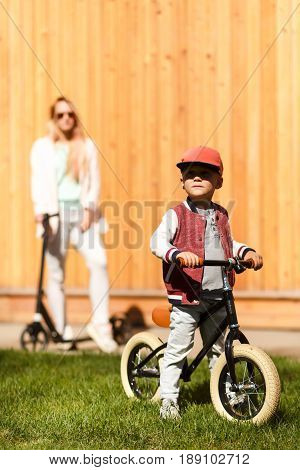 Mother with boy with cycles near wooden wall in park