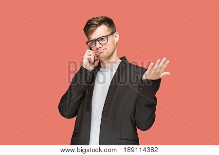 The young caucasian businessman in glasses on red studio background talking on cell phone