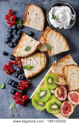 Variety of ingredients for making dessert sandwiches with bread, berries and cream cheese. Red currant, blueberries, sliced kiwi, figs over gray metal background. Flat lay, summer appetizer concept