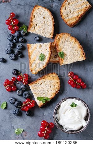 Variety of ingredients for making dessert sandwiches with grilled bread, berries and cream cheese. Red currant, blueberries over gray metal background. Flat lay, summer appetizer concept