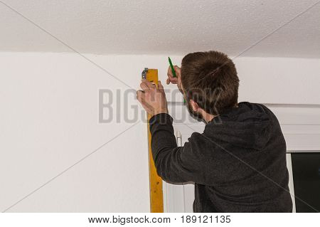 Young craftsman on a ladder with a spirit level and pencil.