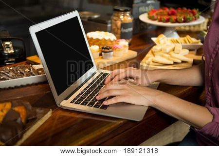 Mid-section of woman using laptop at bakery counter in market