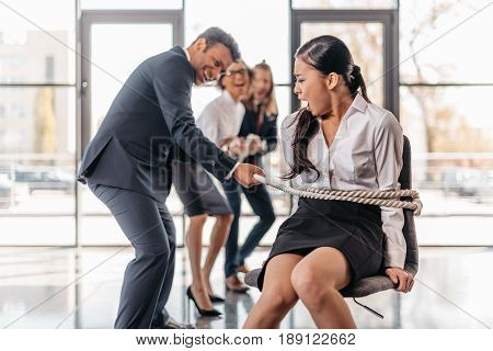 Asian Businesswoman Bound With Rope On Chair And Multicultural Business Team Pulling Her, Team Spiri