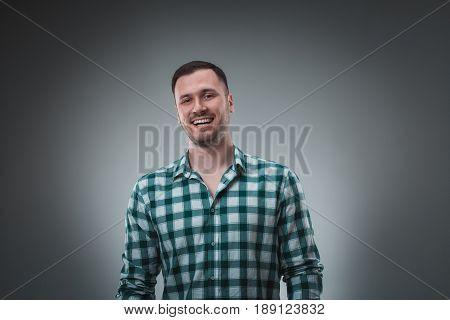 Cheerful man laughing and looking at camera with a big grin. Portrait of a happy young man standing over grey background.