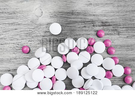 Large white round and small bright pink tablets on a light vintage wooden background at the bottom of the frame.