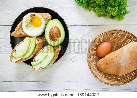 Delicious breakfast - tasty sandwiches with avocado and egg on a dark plate on rustic wooden background. Flat lay. Top view
