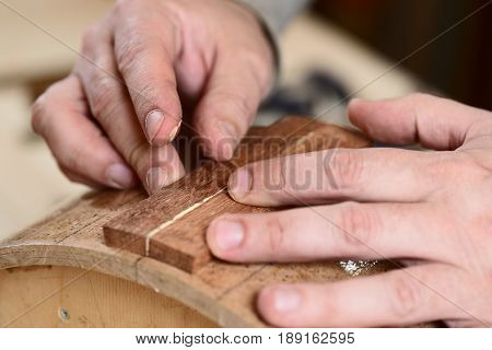 Carpenter glueing wooden parts for drum with bare hands closeup