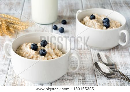 Oatmeal porridge / porridge oats / breakfast cereals with blueberries and bottle of milk on vintage white wooden table. Healthy eating, healthy breakfast food