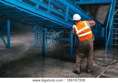 The worker washes the equipment at the waste sorting plant. Waste processing plant. Technological process.