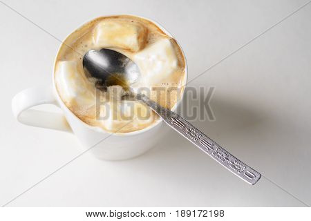 Spoon in a cup of coffee with marshmallows. White mug of hot drink with copy space background.