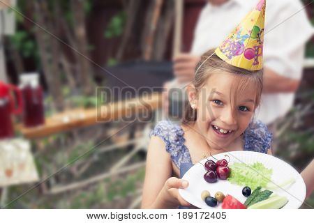 Happy smiling child girl treating healthy eating with plate of vegetables during back yard birthday party