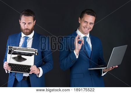 man with beard holding vintage typewriter. Happy businessman smiling with laptop computer ok gesture. model in blue business suit. Old or new. Technology or archaism