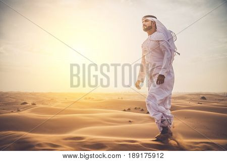 Arabian man walking in the desert at sunrise