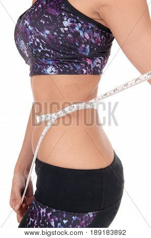 A closeup image of the mid section of a young woman in an exercising outfit measuring her stomach isolated for white background.