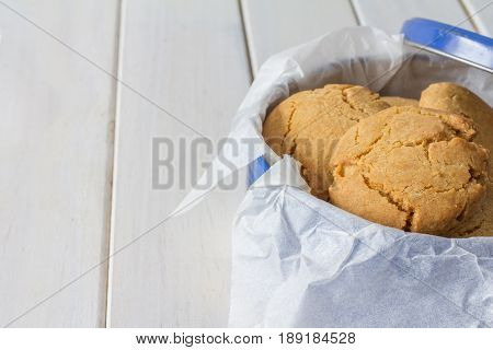 Close Up of Homemade Gingernuts in a Blue Tin on White Wooden Table Horizontal with Copy Space Left