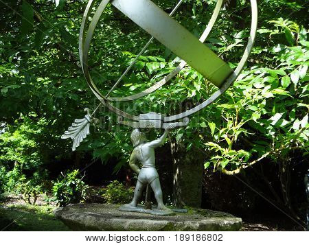 A garden statue, featuring an arrow, globe, and figure on a sunny day.