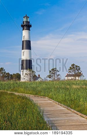 A wooden boardwalk leads through a marsh to the North Carolina's Bodie Island Lighthouse with its bold black and white stripes.