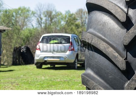 Small the car is compared with big wheel farm machinery standing nearby in the yard.