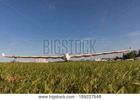 A glider with a protective sleeve parked on a grassy airport on a sunny day.