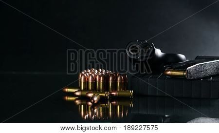 Black hand gun and bullets on the black mirror background.