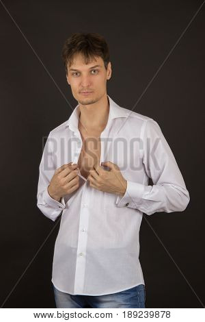 Sexy stylish young man in a white shirt with a black tie and expensive cufflinks on the black background