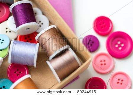 needlework, craft, sewing and tailoring concept - box with thread spools and buttons on table