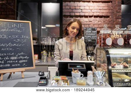 small business, people and service concept - happy woman or barmaid at counter with cashbox working in cafe or coffee shop