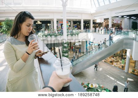 Young woman talking on the phone while walking mall with smoothie, firts-pesron view