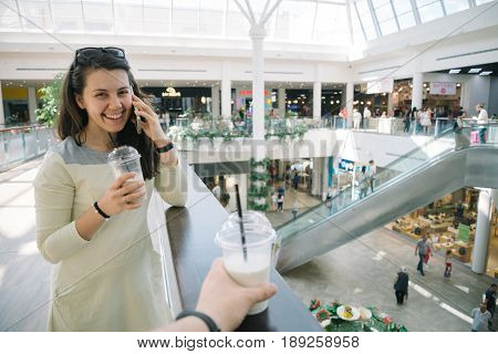 Young woman talking on the phone while walking mall with smoothie, firts-pesron view