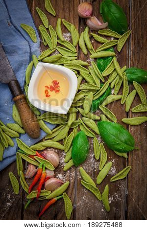 raw italian pasta on wooden board with oilive oil and chili