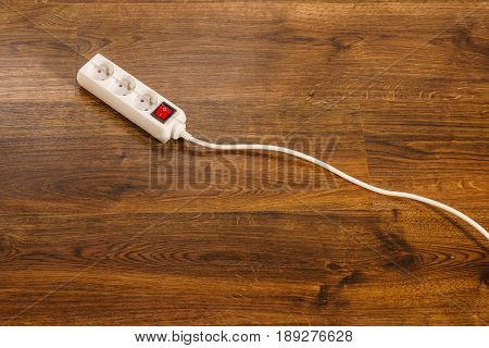 Electricity at home. White electric power strip or extension cord block for extending plug with red switch on off on wooden floor.