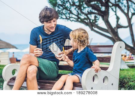 Father And Son Eat Fried Sweet Potatoes In The Park. Junk Food Concept