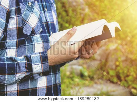 Man reading a book in the park. Student studying memorizing notes outdoors. Young man wearing shirt and reading book. Photo stock.
