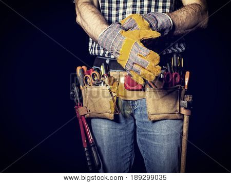detail of handyman with leather toolsbelt and tools on dark background wearing gloves