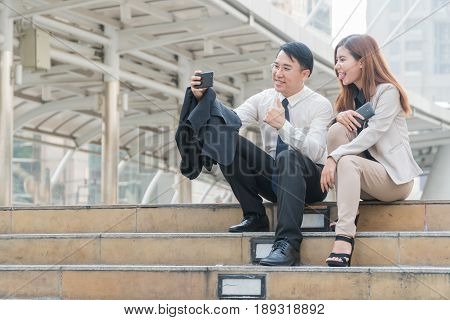 Two businessmen sitting at stair and take self ie with a smart phone in hand on modern city.