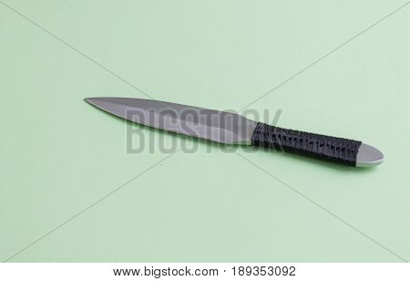 Knife for throwing with a black winding of a handle. On a light green background.