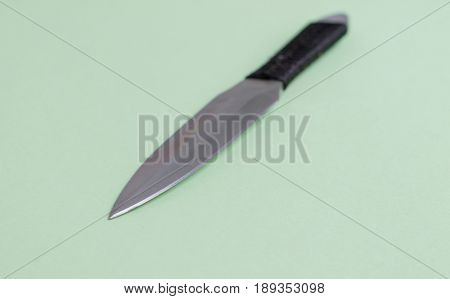Knife for throwing with a black winding of a handle. On a light green background.