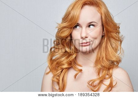  Headshot of doubtful Caucasian freckled female wearing nothingbut red long beautiful hair pouting lips and looking up with indecisive expression on her face showing doubt and hesitation. Body language.