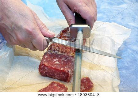 Female hands sharpening chef knife next to salami laid on a wrapping paper