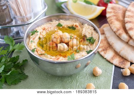 Chickpea paste with chick peas, garlic, cumin, sesami seads, olive oil, coriander in a metal bowl on a green cloth with pita bread and parsley. Traditional food. Healthy eating concept