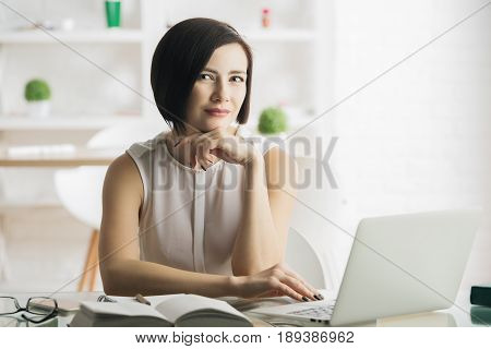 Beautiful thougtful young woman using laptop in modern office