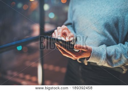 Closeup view of woman holding modern mobile phone in hands.Girl pointing fingers on empty touch mobile screen at night. Horizontal, blurred background, bokeh effects