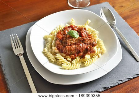Delicious goulash dish on a white plate with basil leaf. Spiral pasta with tomato sauce.
