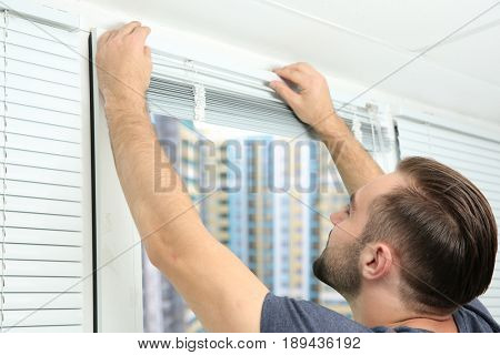 Young man installing window blinds at home