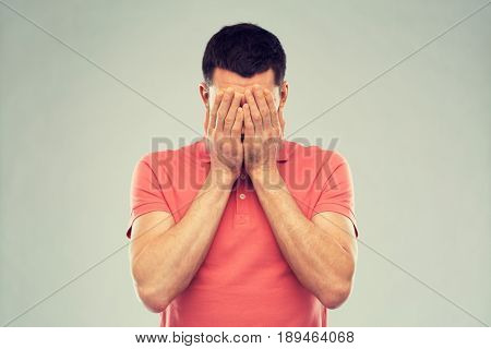 people, crisis, emotions and stress concept - man in t-shirt covering his face with hands over gray background