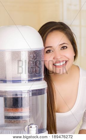 Beautiful woman next to the filter system of water purifier on a kitchen background.