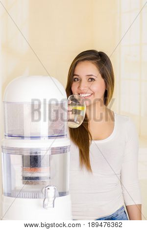 Beautiful woman drinking a glass of water with a filter system of water purifier on a kitchen background.