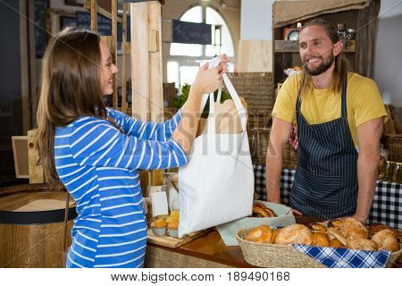 Smiling female customer receiving a parcel from staff at counter in bakery shop