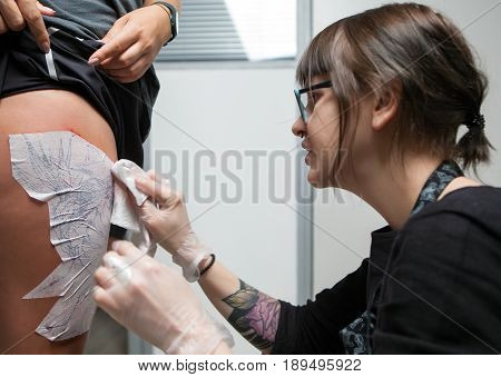 A professional tattooist is presented with sketch on the body of the girl in the Studio. Girl master and model